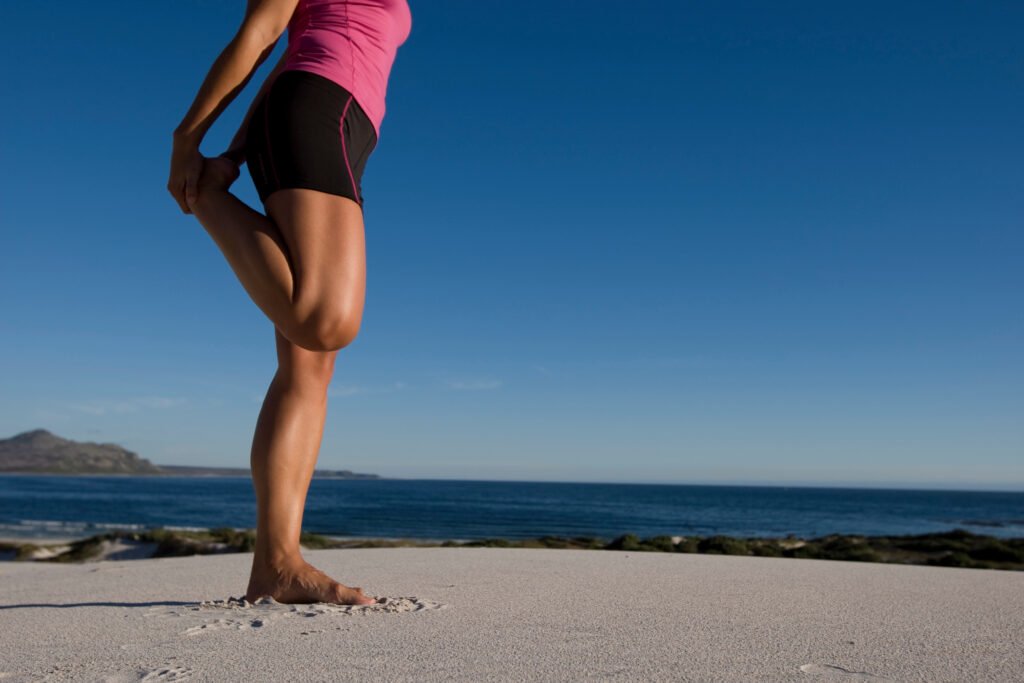 femme en short sur la plage qui s'étire le quadriceps